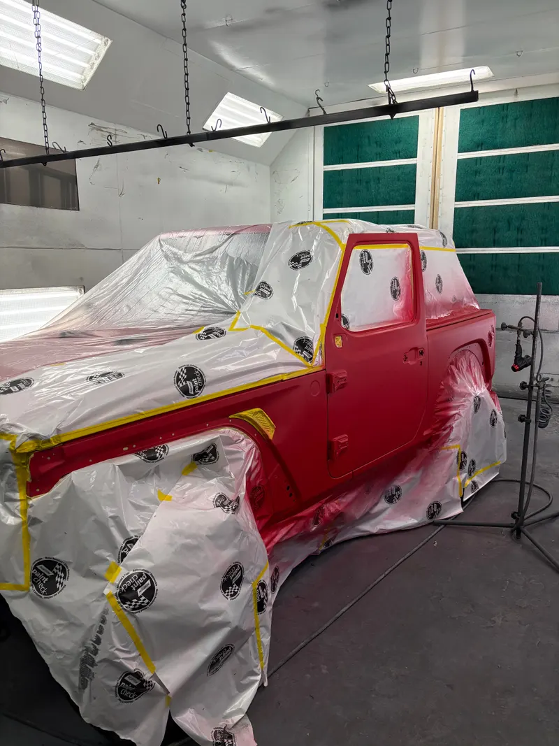 Red Jeep masked with plastic sheeting and tape in the paint booth