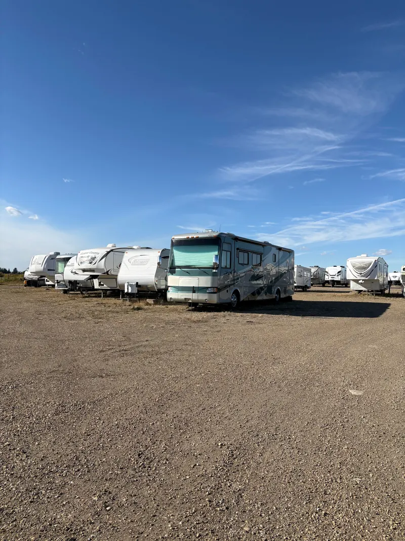 A motorhome parked in a row with fifth-wheel and travel trailers on the gravel lot